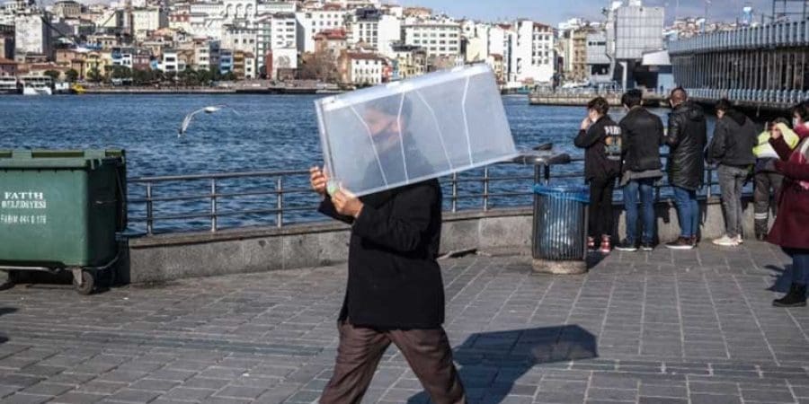 رجل يرتدي قناعًا للوجه ويحمل صندوقًا بلاستيكيا خشية الإصابة بفيروس كورونا (الأوروبية)