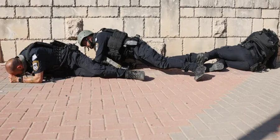 أفراد من القوات الإسرائيلية يحتمون على جانب أحد الشوارع في عسقلان بينما تدوي صفارات الإنذار جراء إطلاق صواريخ من غزة (الفرنسية)